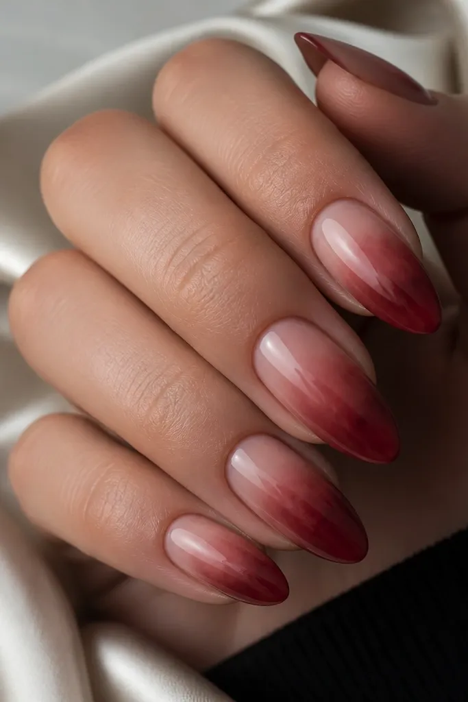 Almond nails with a smoky red fade that looks like soft haze spreading from the tip toward the center, over a nude base. The edges are blurred and cloudy, with a glossy finish.