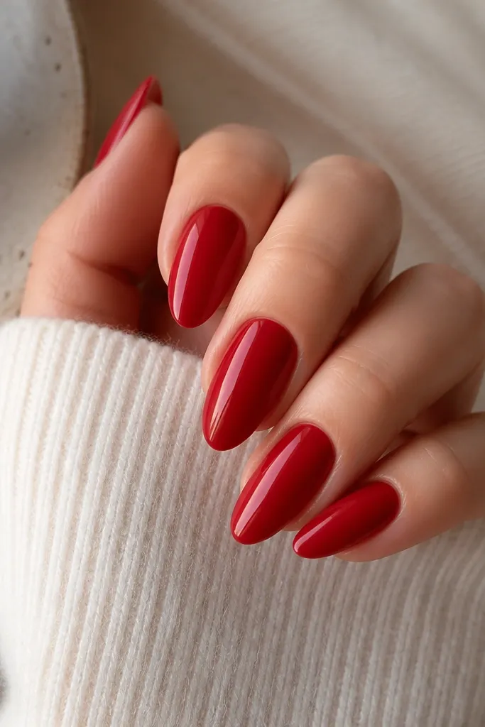 Almond nails painted a true classic red cremé finish. The surface looks smooth and even, with a subtle sheen rather than mirror gloss.