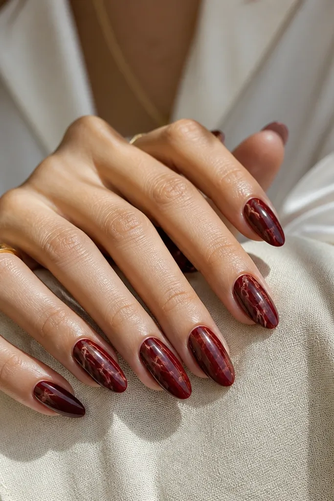 Almond nails with a deep red base and thin lighter red and nude marble veins. The marbling looks organic, with veins branching lightly toward the tip.