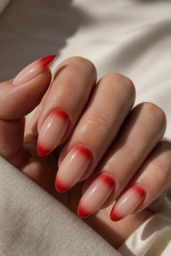 Almond nails with a nude base. There's a red French tip, but instead of a clean line only at the tip, the red blends into a soft half-moon near the cuticle on the same nail, like a gradient mirror.