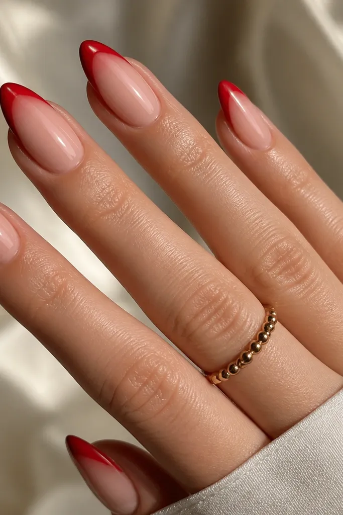 Almond nails with nude base. The French tip is split by a gradient: darker red at the outer corners blending into lighter cherry red at the center. The overall finish is glossy and smooth.
