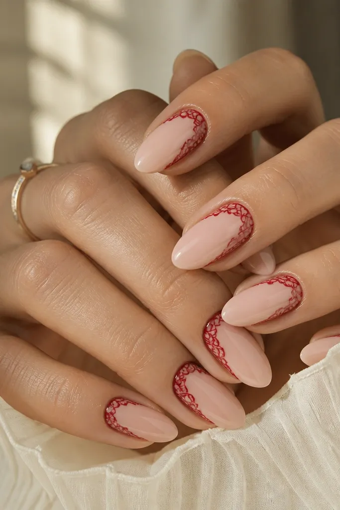 Medium almond nails with a nude base. Fine red lace lines form a V-shape near the cuticle and wrap toward the side edges, leaving plenty of nude space. The lines are crisp and glossy.