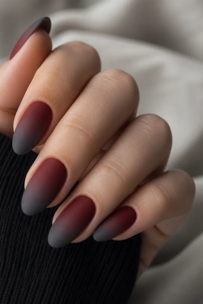 Medium almond nails with a soft matte velvet finish. The base fades from deep red at the cuticle area into a smoke-gray at the tips, with a smooth blended transition and no harsh line.