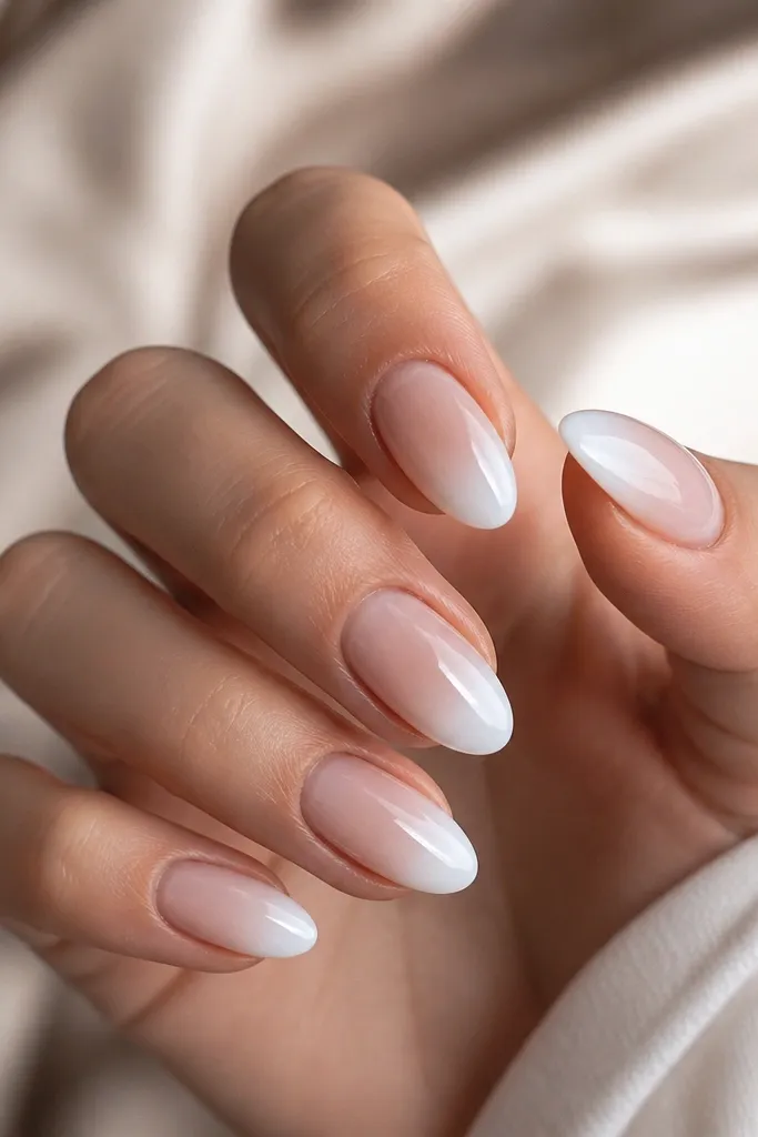 Short almond nails with a nude base that fades into a milky white ombré at the tips; the fade is smooth and airy, glossy top coat.