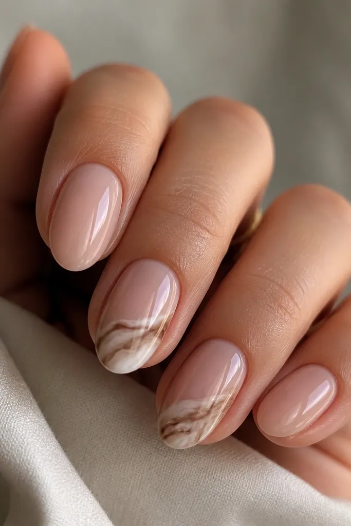 Short almond nails in sheer nude; two nails have a marbled swipe in taupe and off-white across the tip; glossy top coat.