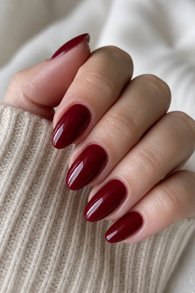 Five short almond nails painted a deep cherry red with a glassy high-shine top coat; the nails look smooth with no nail art, and the cuticles are neatly cleaned.