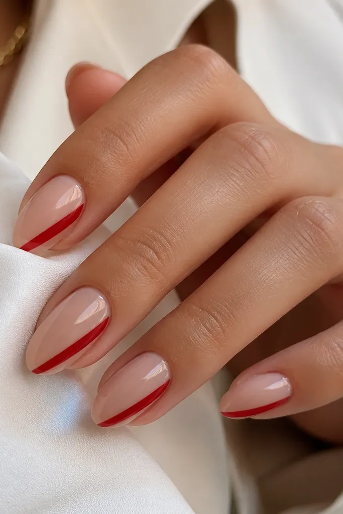 Short almond nails painted nude with a single diagonal side stripe in glossy red on each nail; the stripe runs from lower sidewall toward the tip.