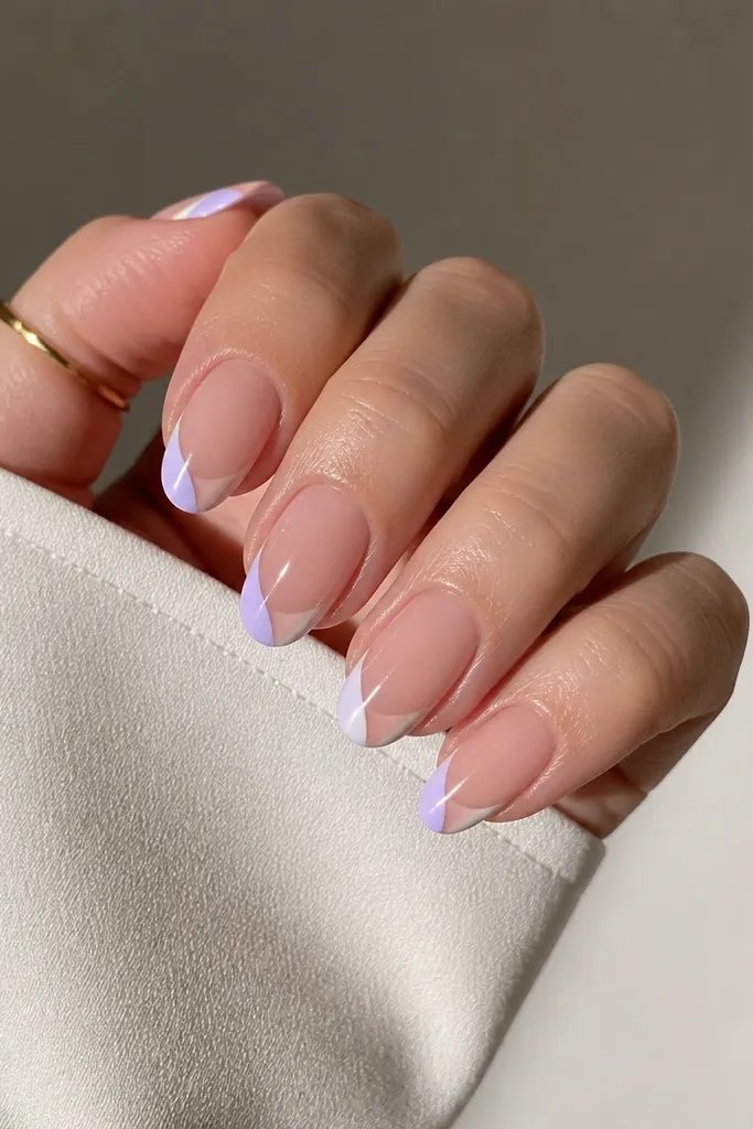 Short almond nails with a sheer nude base; a V-shaped French design at the tip in two colors, white on one side and soft lavender on the other, leaving a V notch of negative space in the center; glossy top coat.