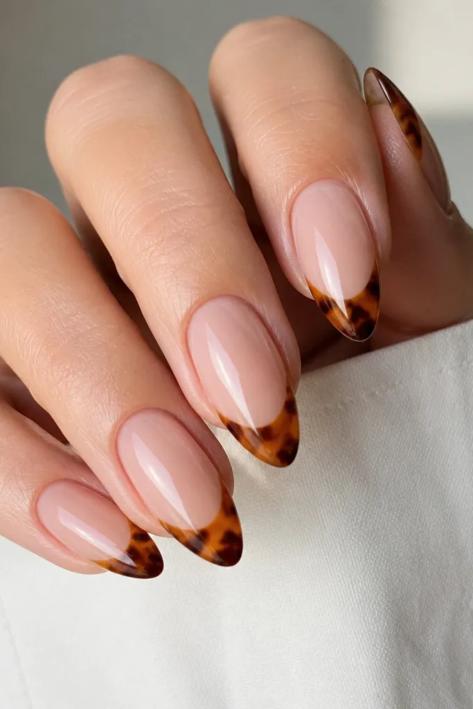 Almond nails with a nude base. The tortoise shell pattern sits only on the tips like a French manicure, with honey and caramel mottling and thin cocoa outlines. The cuticle area is clean and minimal, and the tips are glossy and defined.