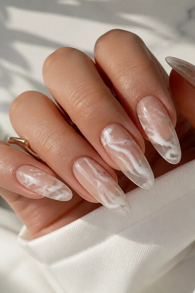 Long oval extensions with a clear base showing through. White marble swirls run diagonally across the nails, with a glossy finish and a few thin gray lines for realism.