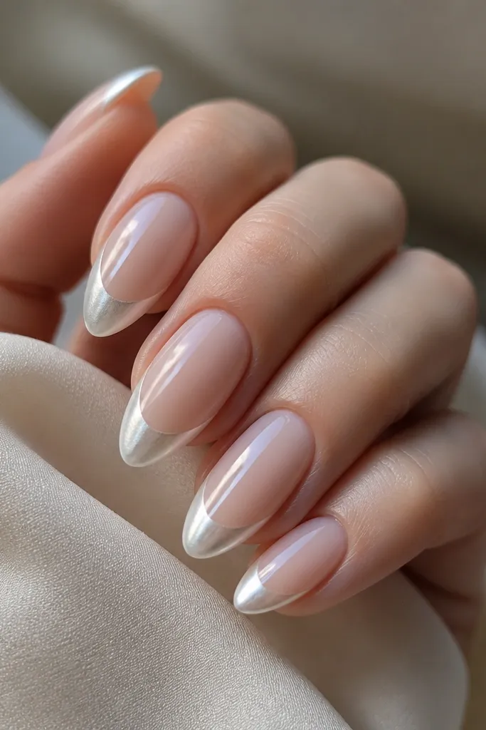 Almond nails with a foggy milky nude base. The tips have a crescent shape in white chrome powder that looks metallic but soft, finished with a glossy top coat.