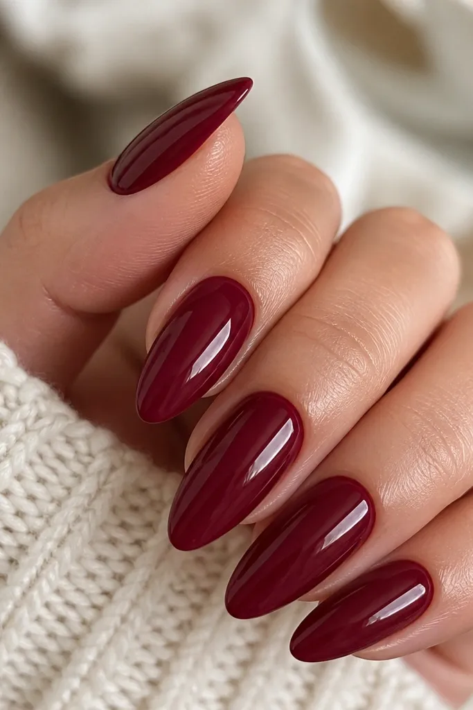Close-up of almond-shaped nails painted in a deep wine red crème finish with a glossy top coat; the cuticles are clean and the color looks uniform from base to tip.