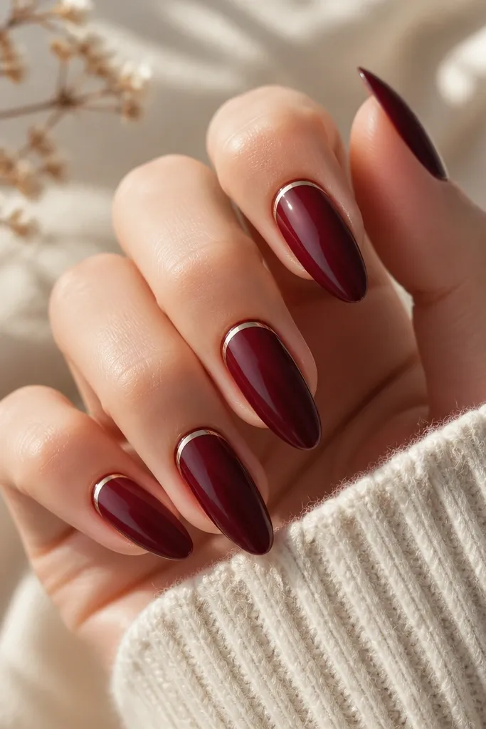 Almond nails in deep wine red with a thin curved halo line around the cuticle in a subtle rose-gold tone; glossy finish with sharp edges.