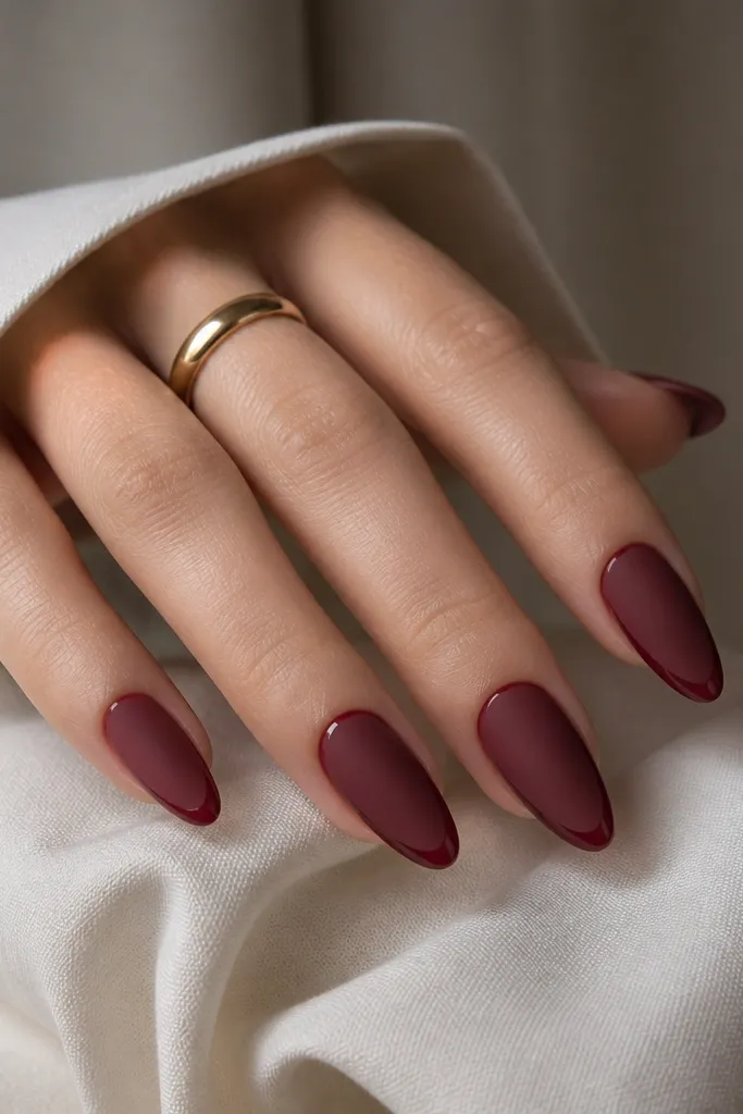 Almond nails painted matte wine red, with a super thin glossy French line near the tip in the same wine shade; the contrast is subtle and crisp.