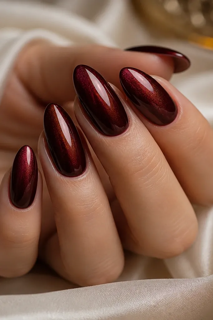 Almond nails with a deep wine red base and a fine chrome dust effect that looks like smoky burgundy metal; high shine finish with smooth reflection.