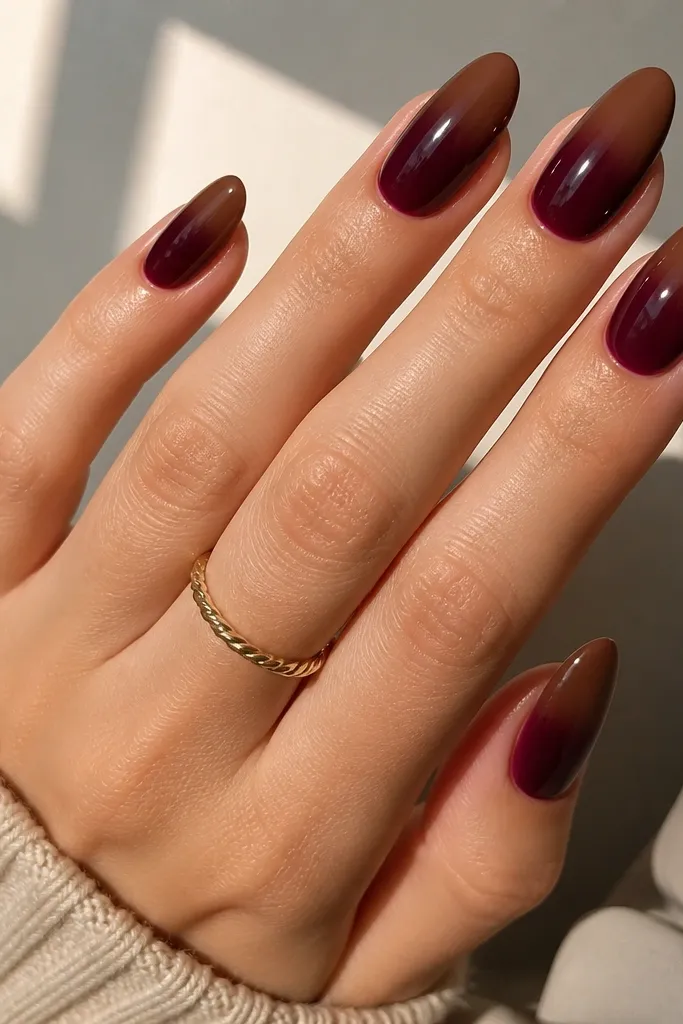Almond nails with an ombre that transitions from wine red at the base into a cocoa-brown tint toward the tips; glossy finish, smooth blend.