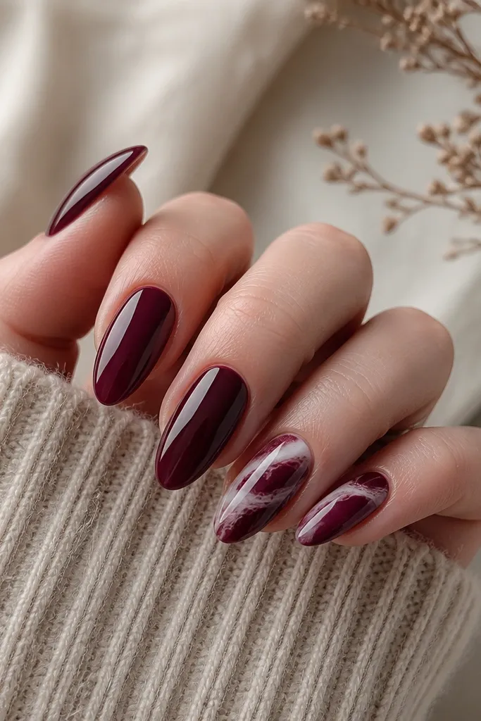 Almond nails in wine red with one or two accent nails showing thin white and deep burgundy marble veins; glossy finish with a realistic veined pattern.