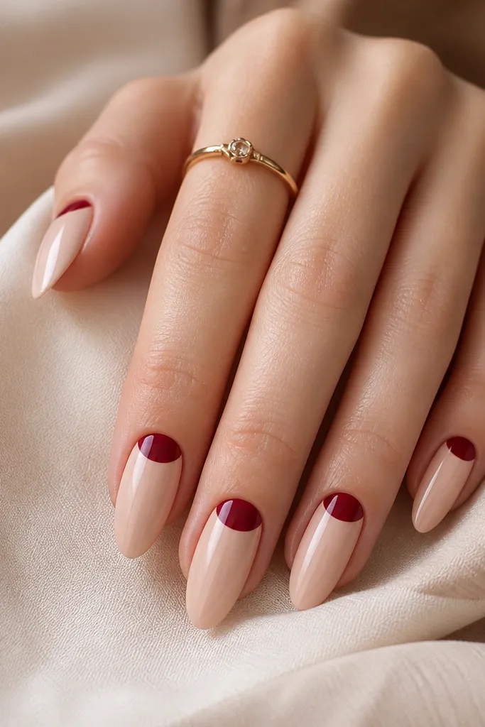 Almond nails with nude base and a half-moon cutout at the cuticle; the half-moon area is painted wine red with clean edges and glossy finish.