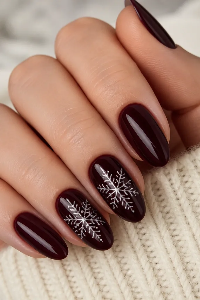 Medium almond nails in a deep black cherry shade with a high-gloss finish. Two nails show detailed silver snowflakes with tiny dot fills in the branches. The snowflakes are centered and crisp, and the rest of the nails are plain glossy black cherry.
