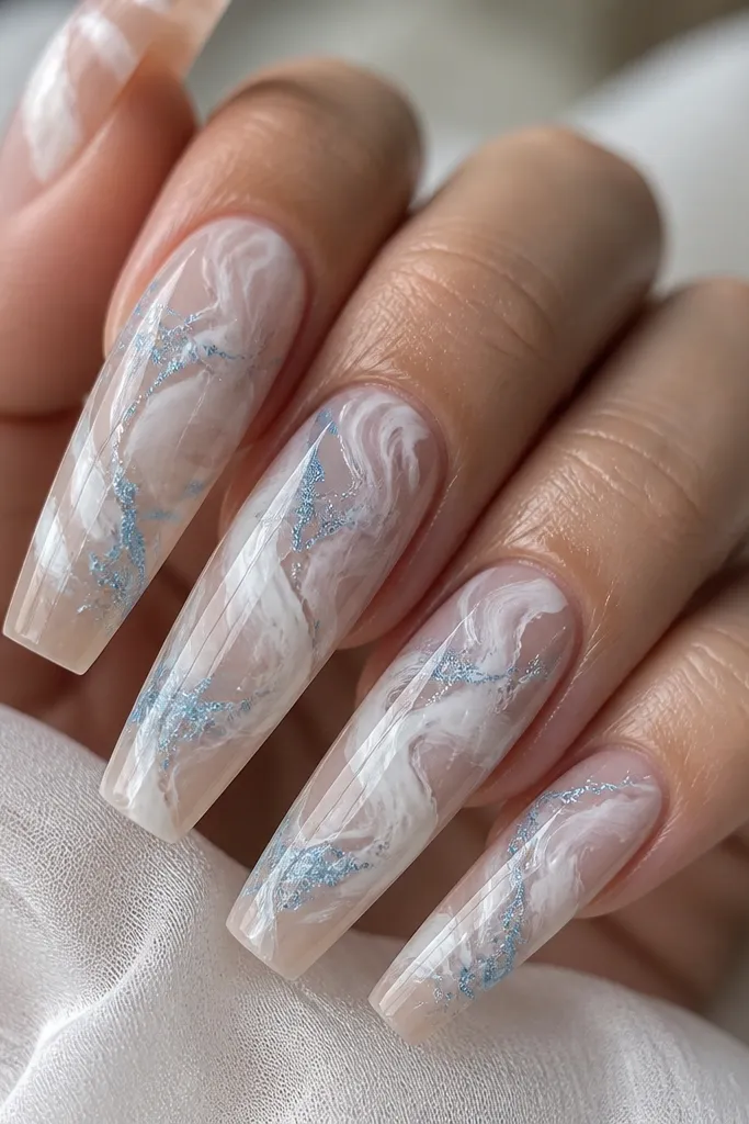 Long coffin nails with white marble swirls over a sheer nude base. Blue glitter veins run through the marble like icy cracks. The overall finish is glossy and smooth, and the blue sparkles look embedded in the design, not sitting on top.