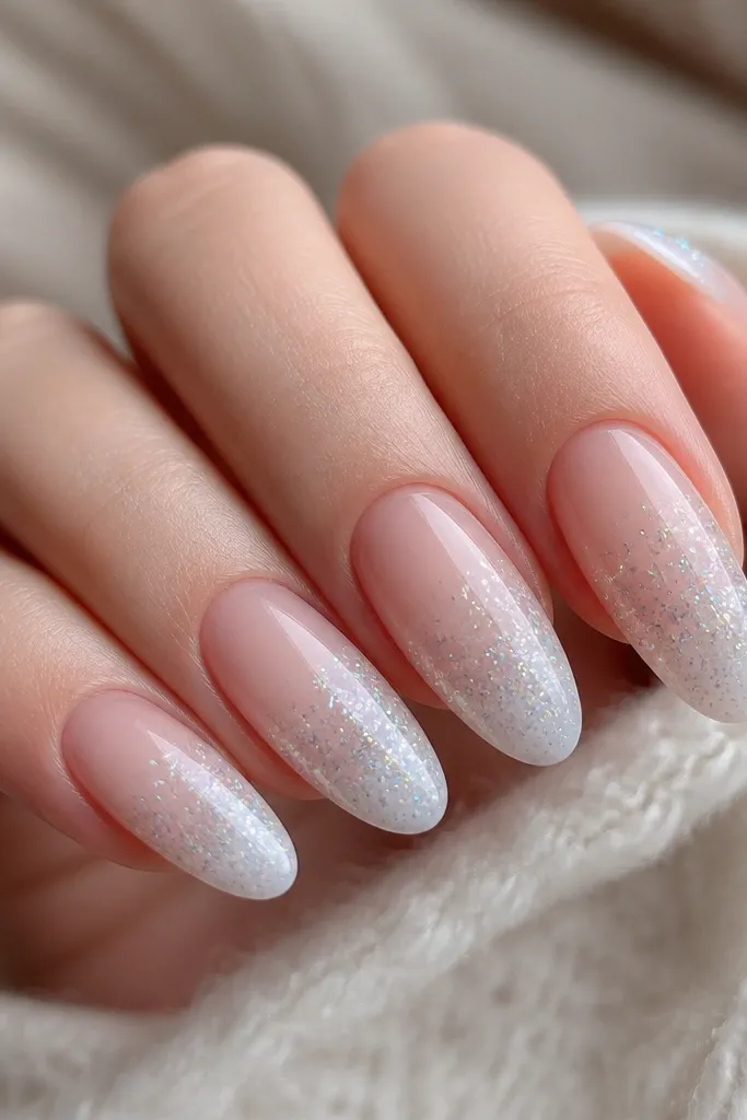 Close-up of medium almond nails with a milky nude base fading into icy white. The sparkle is fine holographic star dust concentrated on the outer third and the tips, with a glossy gel top coat.