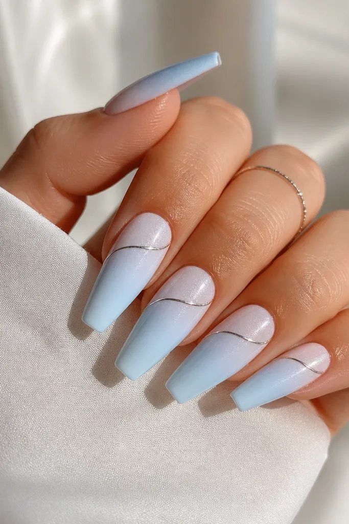 Coffin nails with a light blue ombre fading into white. A thin silver chrome line runs diagonally near the smile line, and the rest has subtle shimmer.