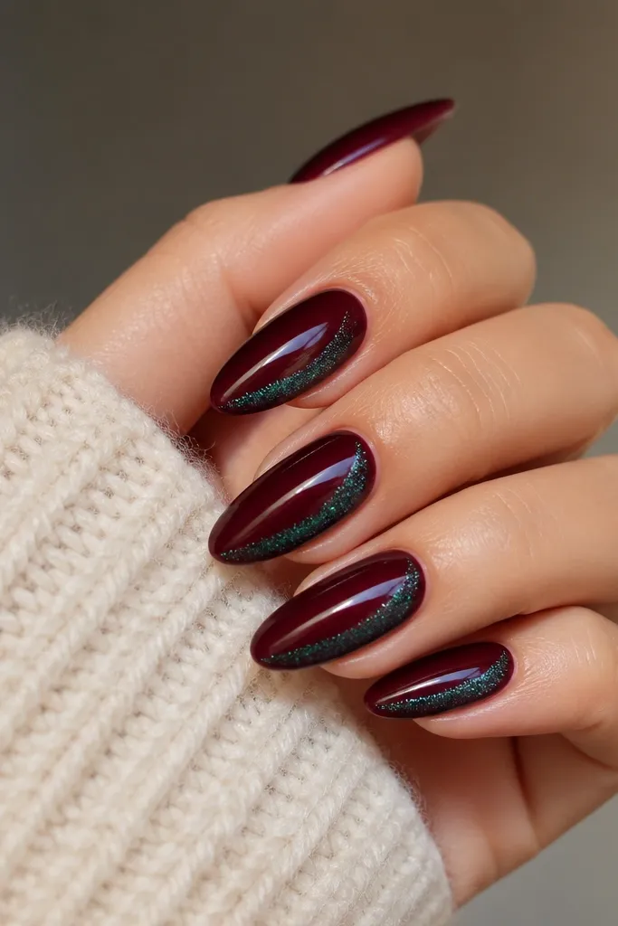 Almond nails in deep burgundy gloss. Inside the inner edge near the tip, there are teal glitter streaks that curve upward slightly, like an inner highlight. The outside edge stays solid burgundy.