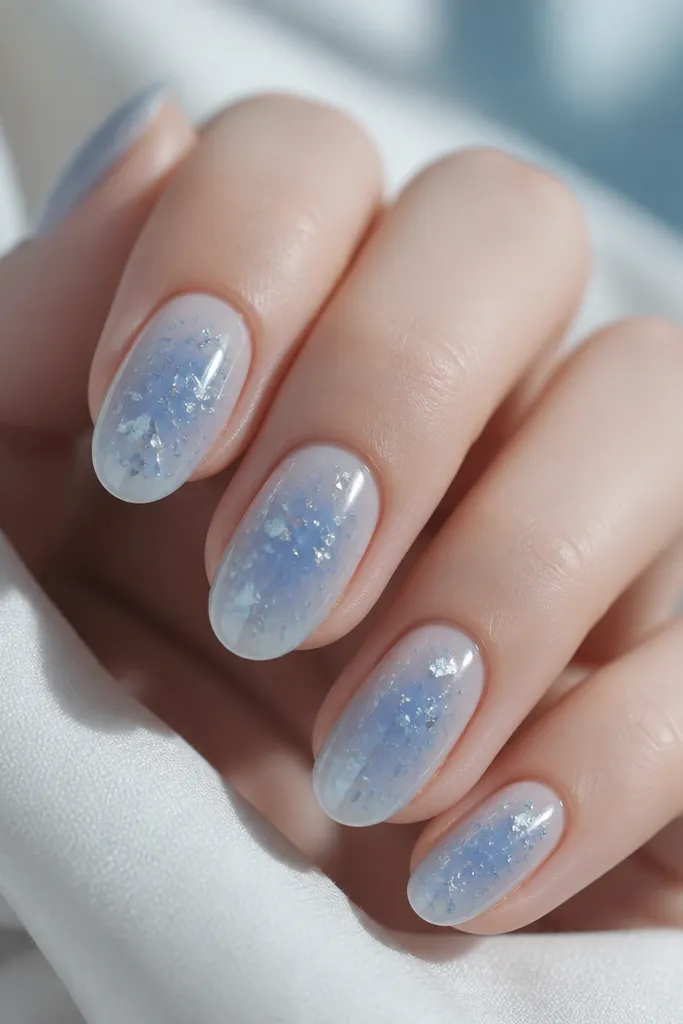 Icy blue nails with a smooth glazed gradient. Silver foil flakes are scattered like tiny ice crystals, with a glossy reflective top coat.