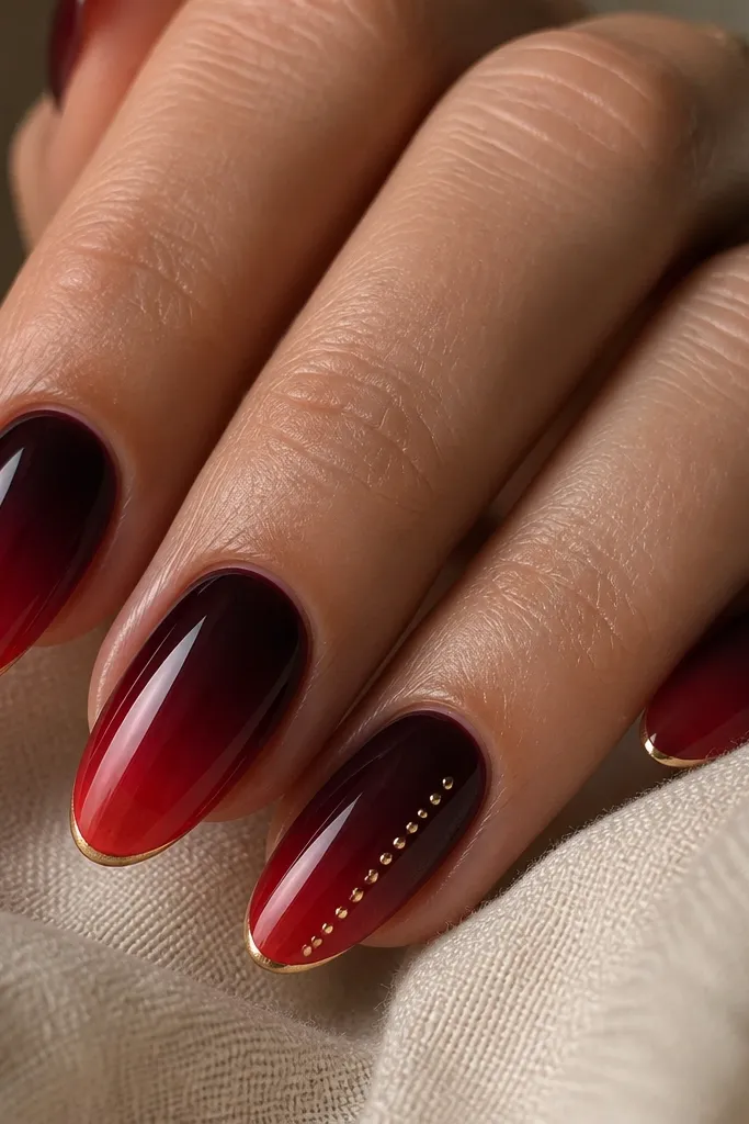 Nails show an ombre fade from deep wine at the cuticle into sheer red at the tip, all glossy. Along the very edge of the tip there is a thin 'glow' line in pale gold, and one nail has a tiny gold dot trail like lights.