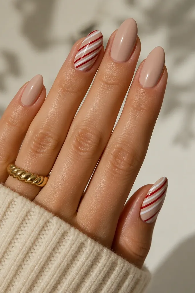 Almond nails with a creamy nude base. One or two nails have a diagonal candy-cane stripe in white and red, with the remaining nails plain glossy nude.