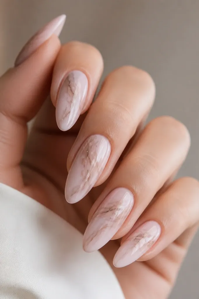 Almond nails with a glossy pale pink base. Each nail has a soft marble swirl in nude beige and faint warm gray, like thin smoke lines. The marble stays mostly in the center and fades toward the sidewalls.